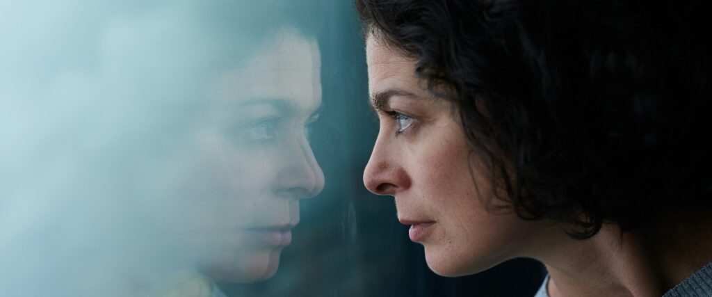 A person gazes out of a foggy window, with blurred reflections and soft light creating an introspective atmosphere.