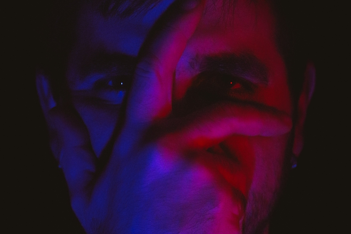 A dimly lit scene with contrasting shades of purple and blue, highlighting the silhouette of a person’s ears and neck.