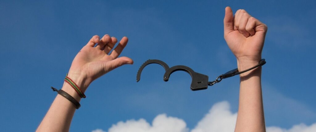 Two hands in the air with handcuffs on one hand