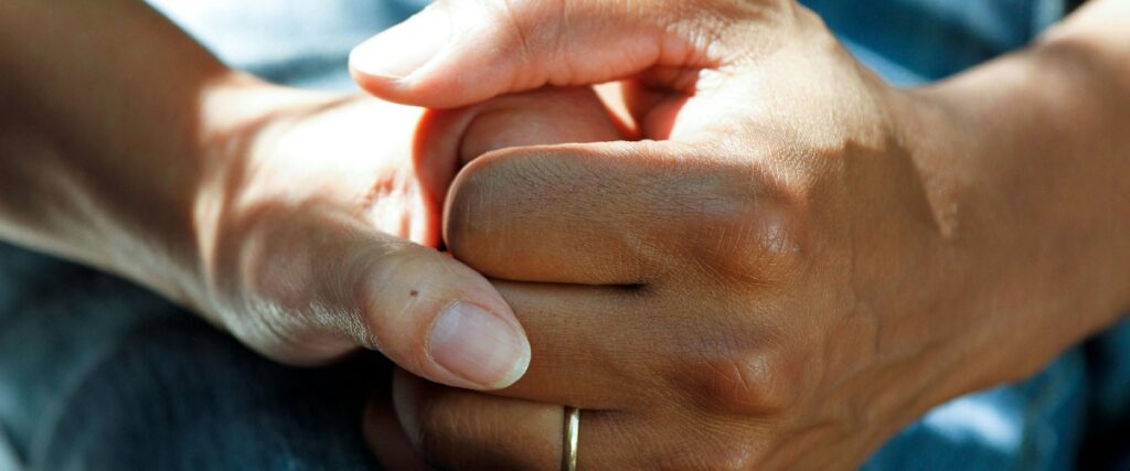 Close-up of two hands clasped together, showcasing diverse skin tones and natural nails.