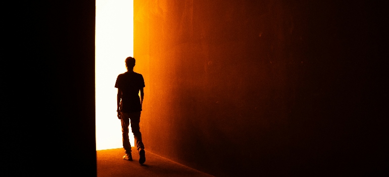 A silhouetted figure walks towards a bright, glowing doorway, framed by dark walls, symbolizing hope or a new beginning.