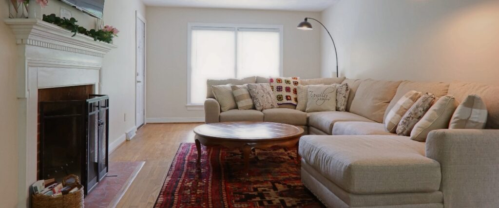 Cozy living room featuring a sectional sofa, round coffee table, and a fireplace, with warm lighting and colorful pillows on a patterned rug.