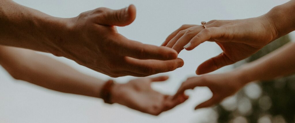 Two hands reach towards each other, one adorned with a ring, symbolizing connection and intimacy against a soft, blurred background.