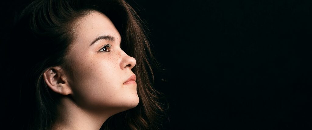 Profile view of a woman with long, dark hair against a black background, showcasing her ear and flowing locks.
