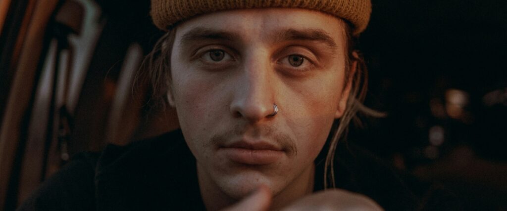A person wearing a cozy knit hat sits in a car, illuminated by soft ambient light, creating an intimate and reflective atmosphere.