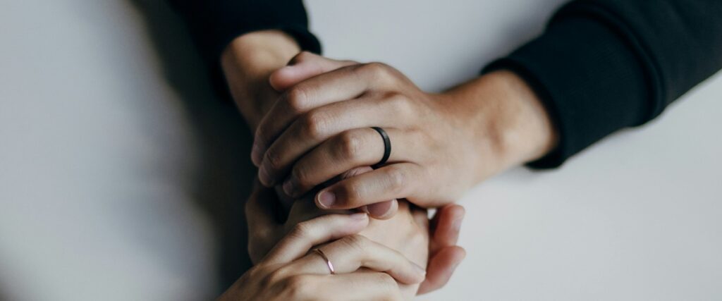 Two pairs of hands gently clasped together, showcasing wedding rings and a sense of connection and mutual support.